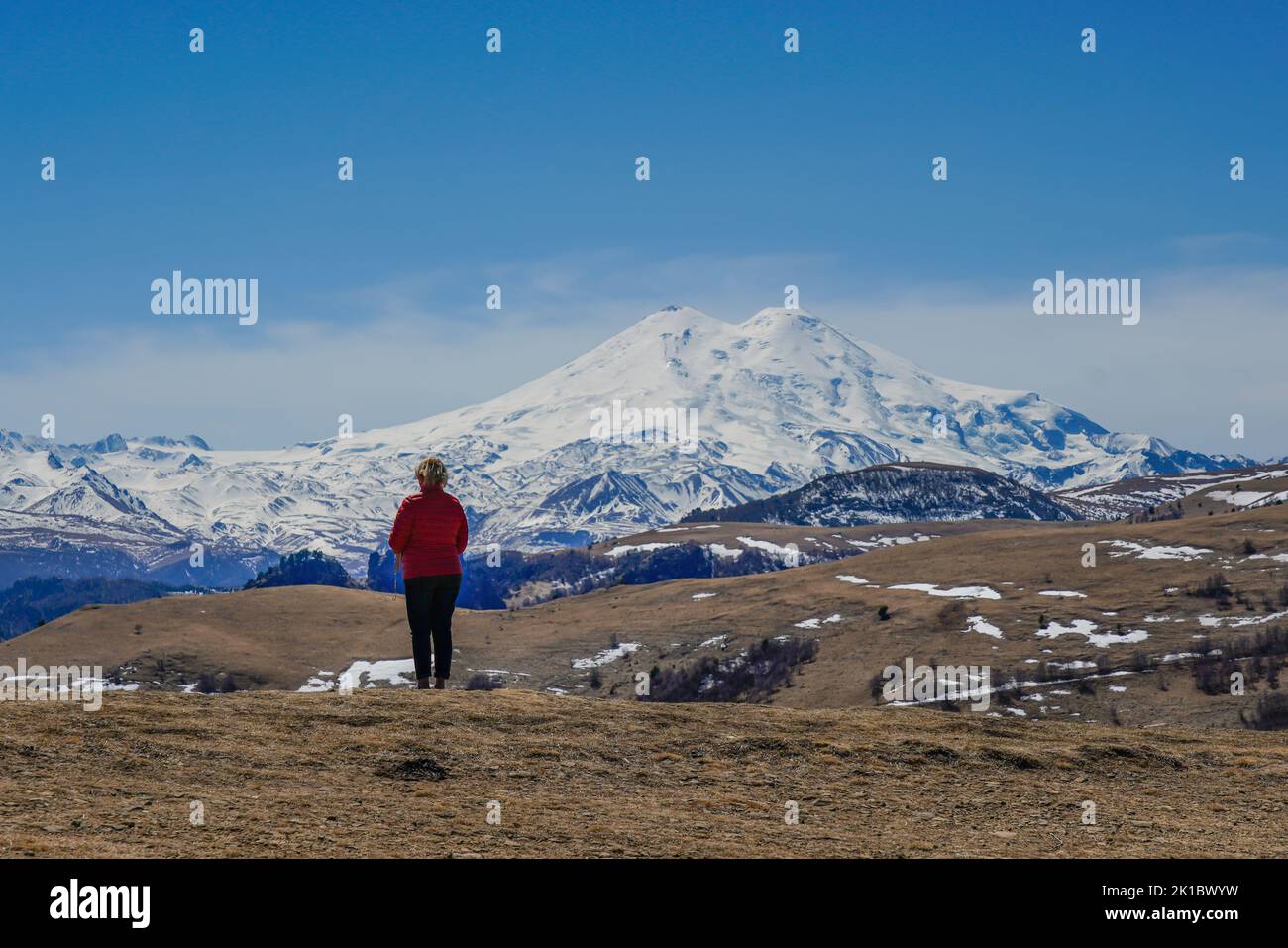 Panorama of Mount Elbrus against the backdrop of the Main Caucasian Range. bckview of a woman, Karachay-Cherkessia. Russia. Stock Photo
