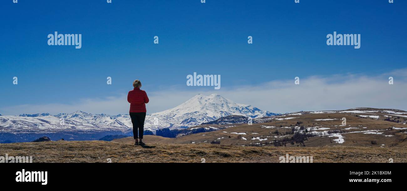 Panorama of Mount Elbrus against the backdrop of the Main Caucasian Range. back view of a woman, Karachay-Cherkessia. Russia. Stock Photo