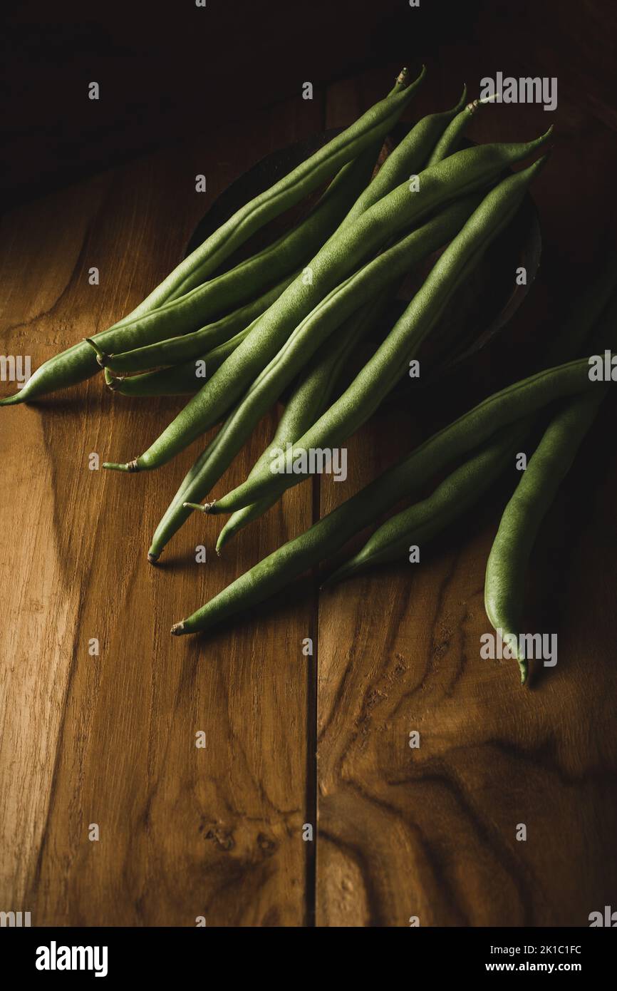 green beans on a wooden surface, also known as french beans, string beans or snaps, freshly harvested vegetable taken in dark moody background Stock Photo