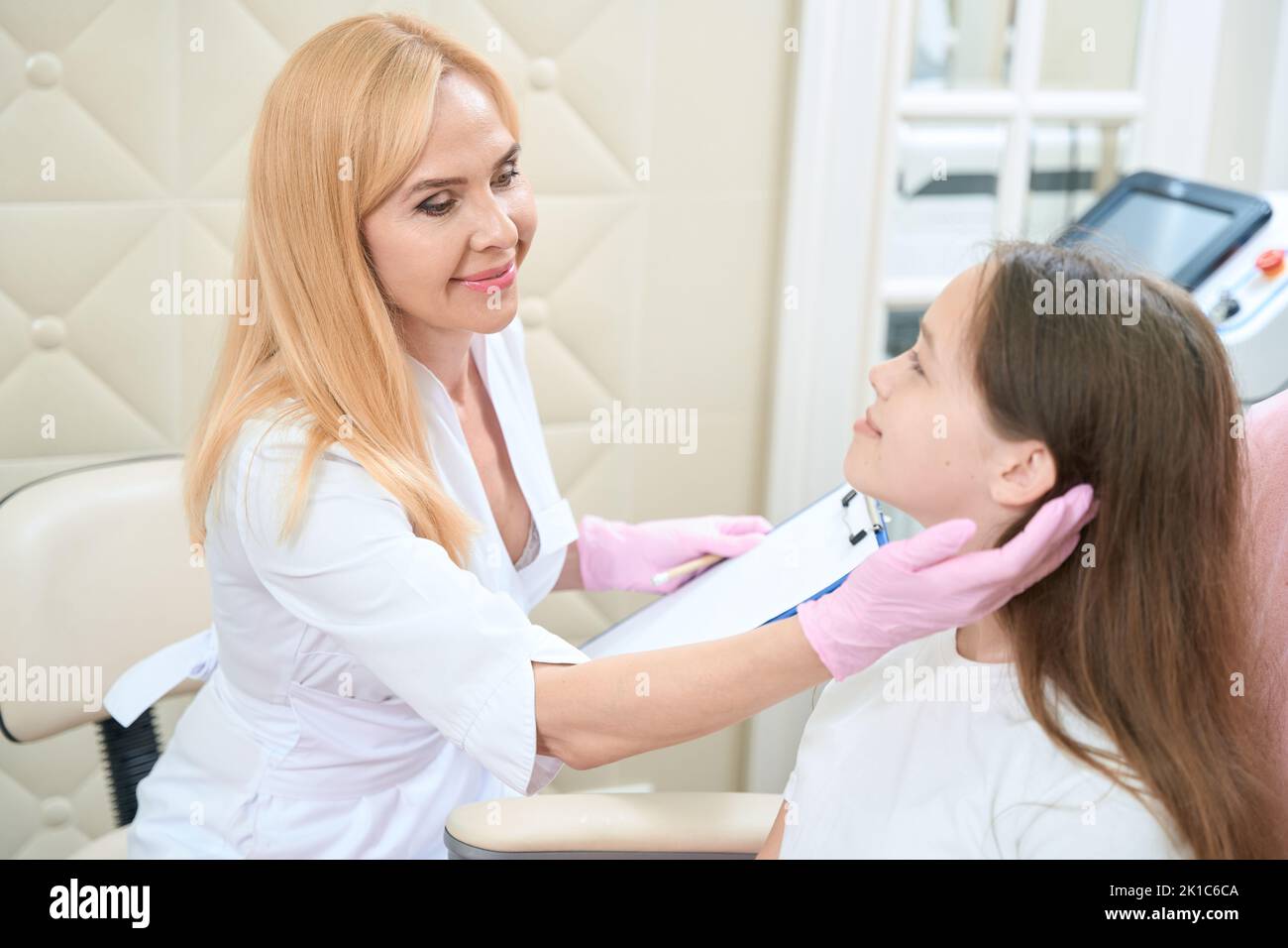Smiling female dermatologist examining girl face in beauty parlor Stock