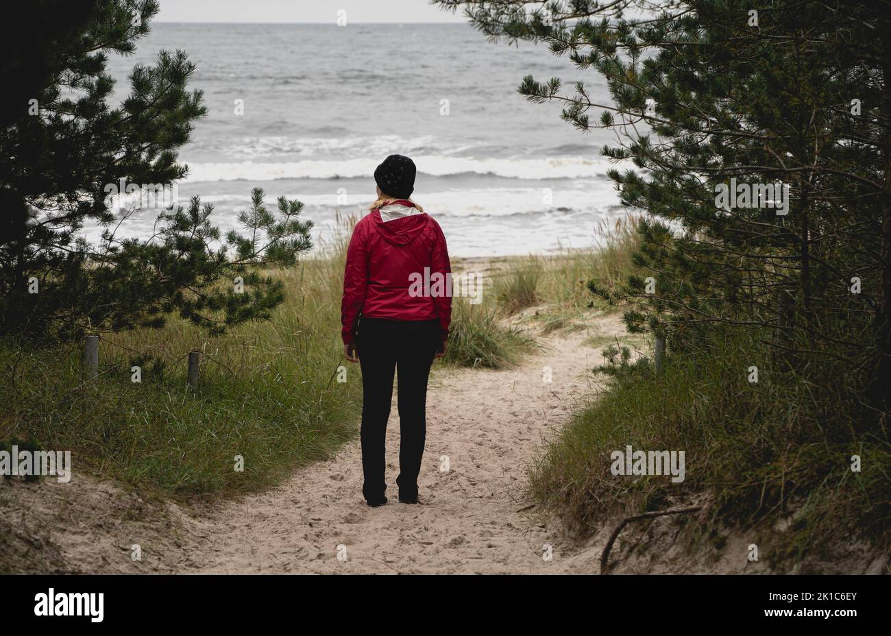 Woman in red standing on the sandy beach on the Baltic Sea, Ruegen Island, Germany Stock Photo