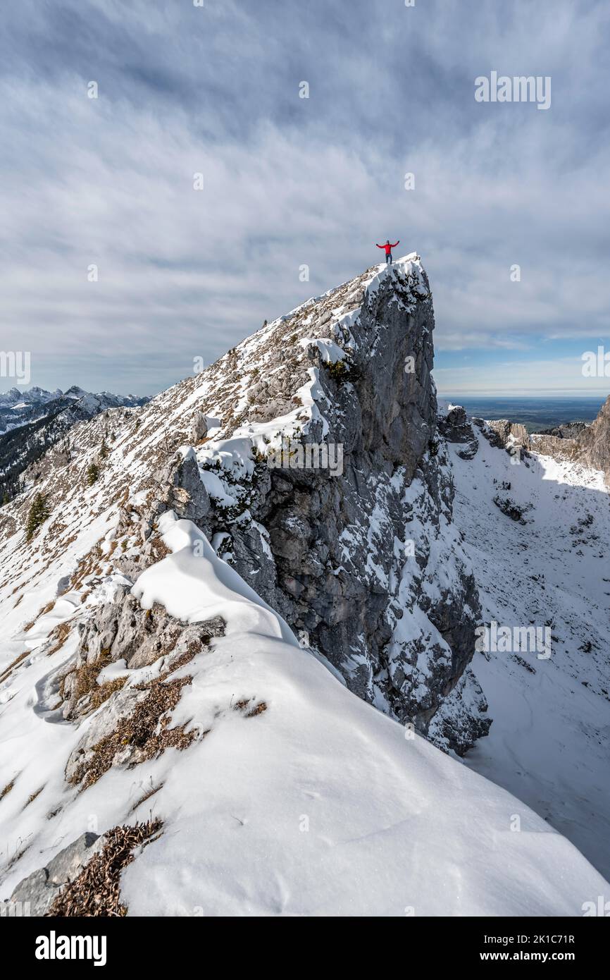 Mountaineer stretching his arms in the air, standing on a snow-covered rocky ridge, Fensterl on the hiking trail to Ammergauer Hochplatte, in autumn Stock Photo