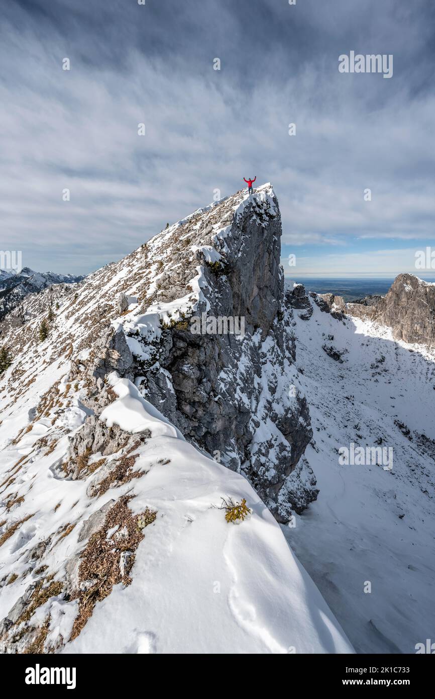 Mountaineer stretching his arms in the air, standing on a snow-covered rocky ridge, Fensterl on the hiking trail to Ammergauer Hochplatte, in autumn Stock Photo