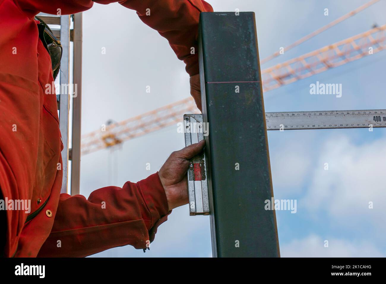 A skilled worker measures and marks a line on a square pipe with an