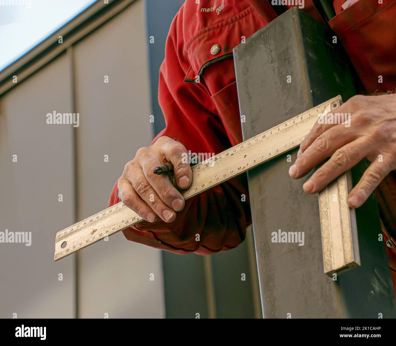 A skilled worker measures and marks a line on a square pipe with an