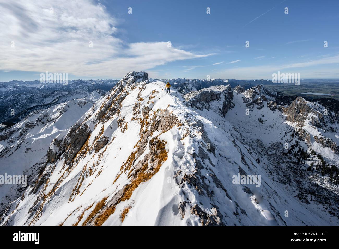 Climbers on a narrow rocky snowy ridge, behind peak crow, view of mountain panorama, hiking to Ammergauer Hochplatte, in autumn, Ammergau Alps Stock Photo