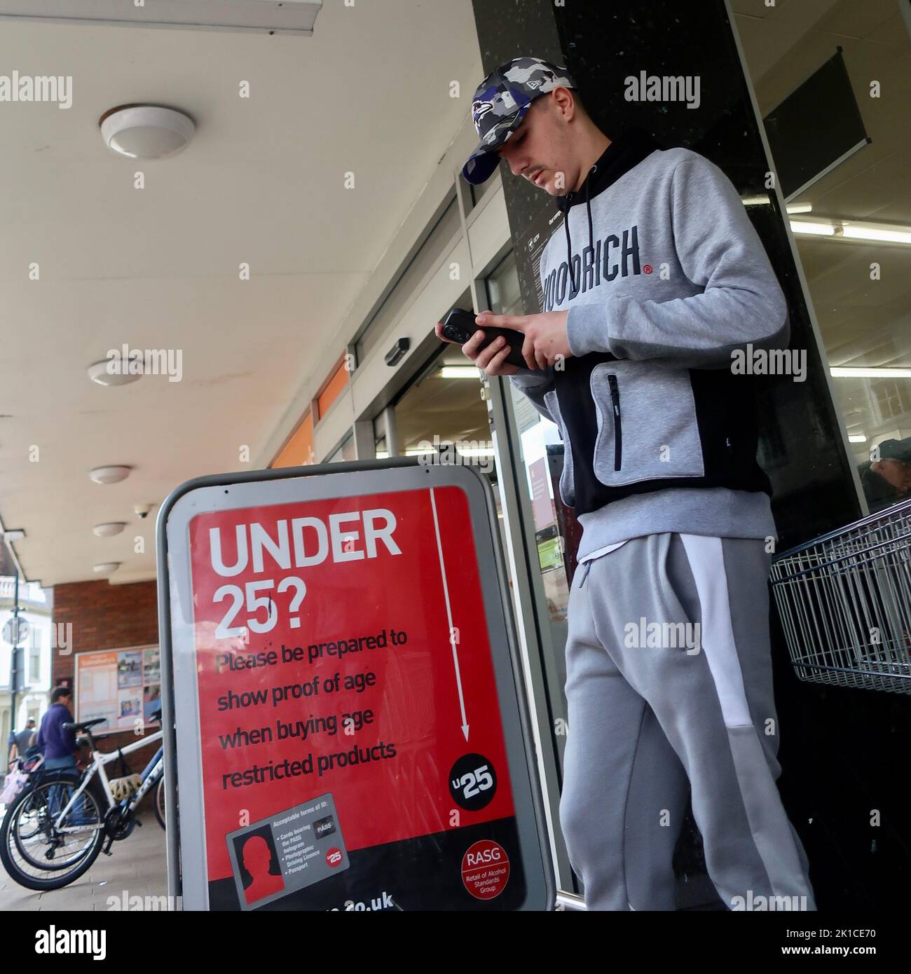 Ipswich, Suffolk, UK - 17 September 2022 : Young man coming out of Sainsbury’s by a sign advising if you are under 25 ID will be required before buying age restricted goods. Stock Photo