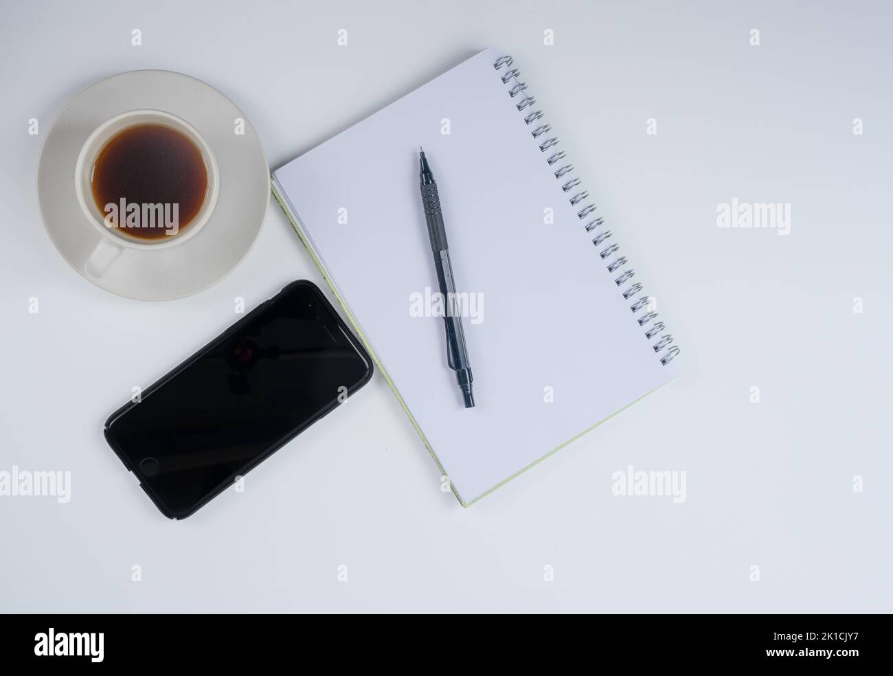 cup of hot coffee mobile phone note pad and pen on a white desk Stock Photo