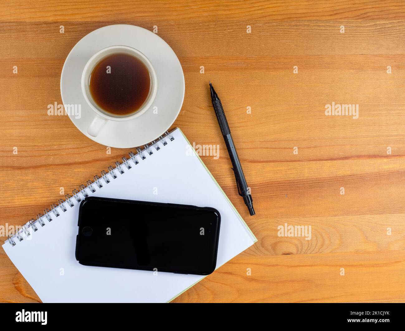 cup of hot coffee mobile phone note pad and pen on a wood desk Stock Photo