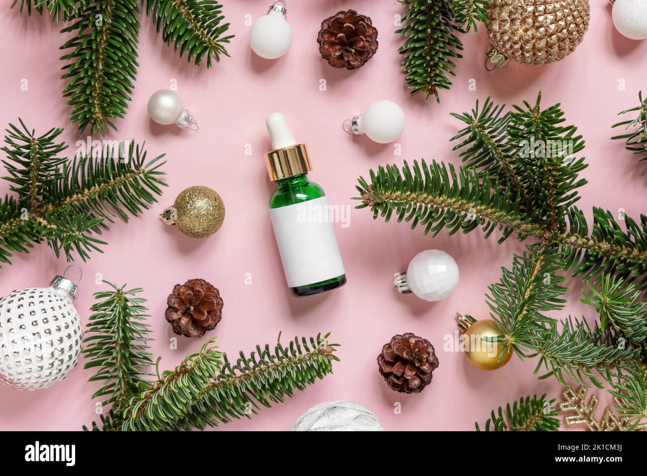 Green Dropper Bottle near Christmas decorations, fir branches and pine cones on pink top view. Holiday brand packaging mockup. Skincare beauty product Stock Photo