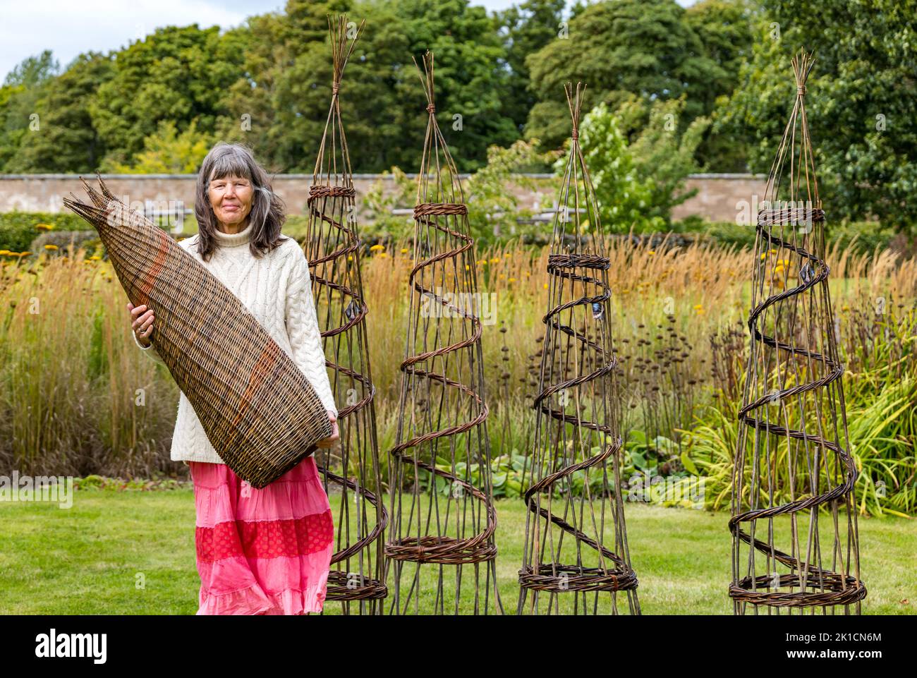 Amisfield Walled Garden, East Lothian, Scotland, UK, 17th September 2022. Art in the Garden: an exhibition of artwork by artists with differing styles and materials takes place for a week. Pictured: weaver Lise Bech with some of her woven willow work including obelisks; the woven basket she holds is made from 3 kinds of willow grown in the garden. Credit: Sally Anderson/Alamy Live News Stock Photo