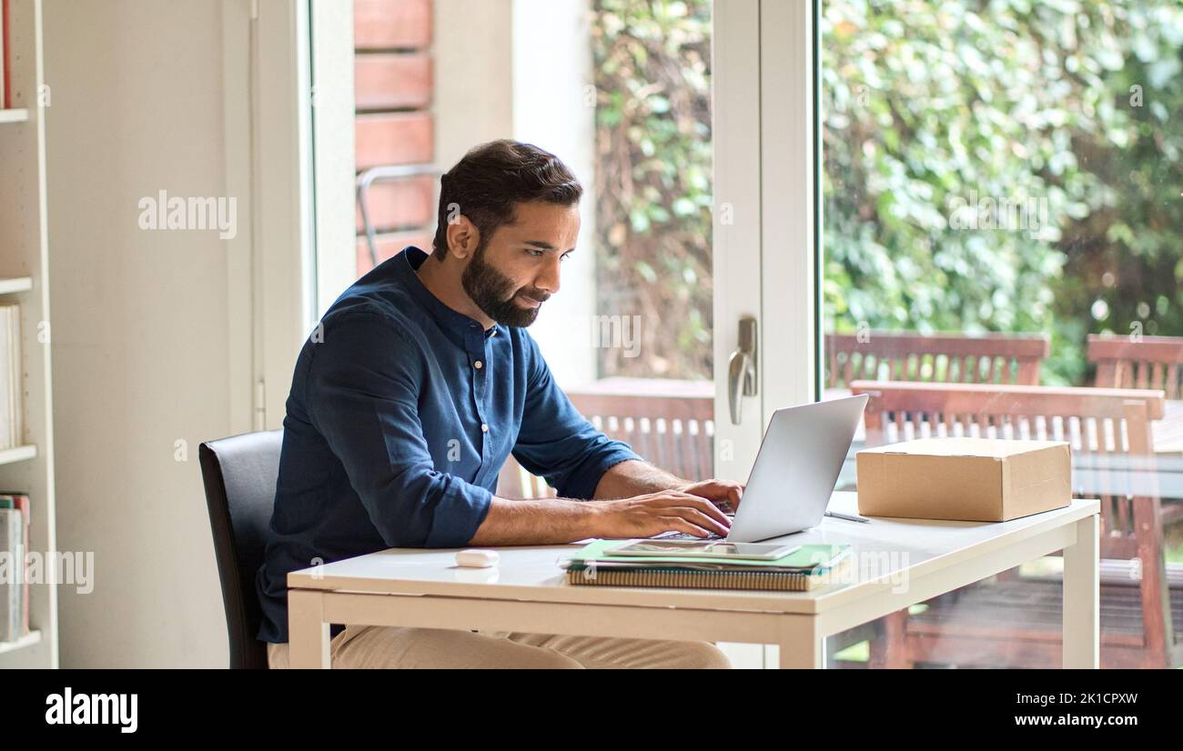 Indian business man remote working on laptop computer sitting at home office. Stock Photo