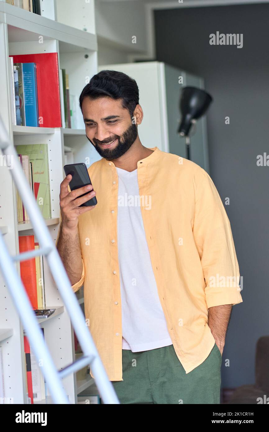 Indian man using phone standing at home checking e books in bookshop. Stock Photo