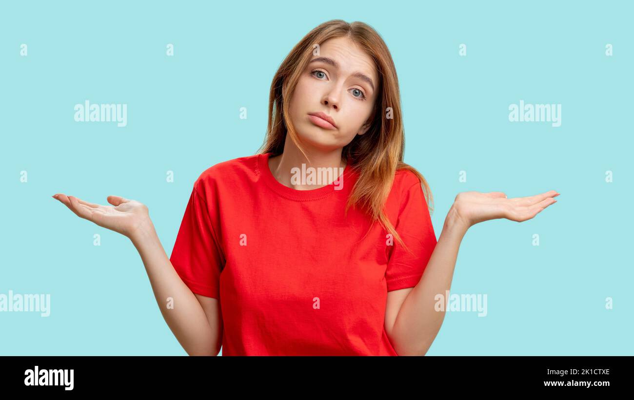 Clueless woman portrait. Whatever gesture. Indifferent lady in red t-shirt shrugging isolated on blue background. No idea. Who cares. Fail sorry. Stock Photo