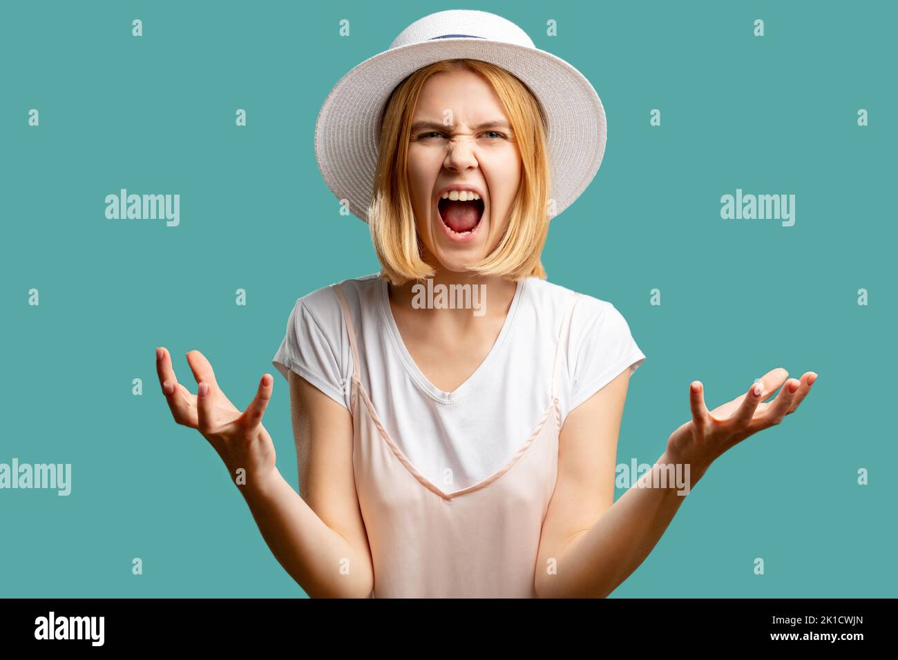 Furious woman. Feeling rage. Angry screaming lady in white summer outfit looking at camera isolated on green. Canceled vacation. Overwhelmed hate. Neg Stock Photo