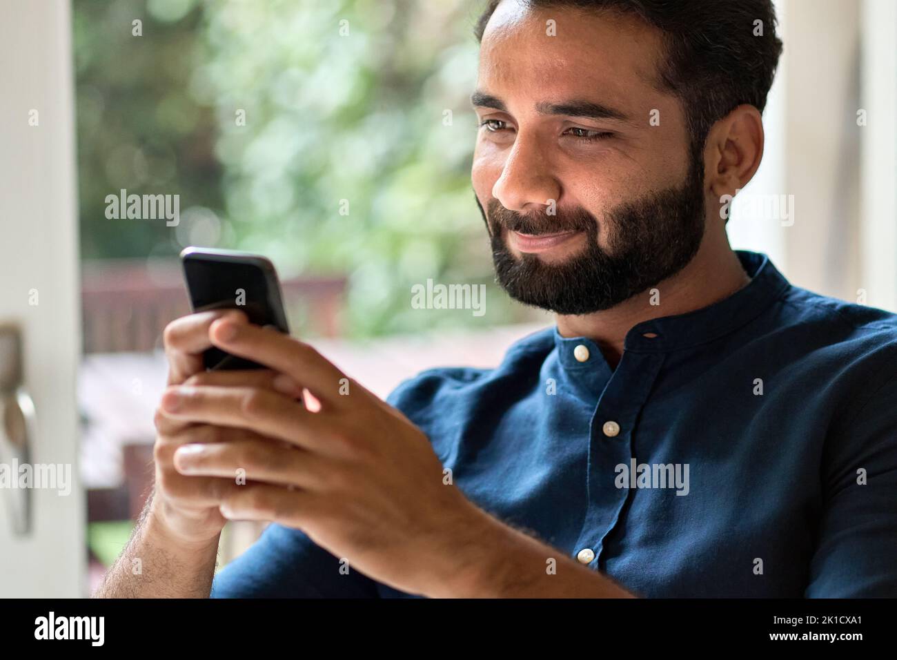 Indian man holding smartphone using mobile phone at home. Stock Photo