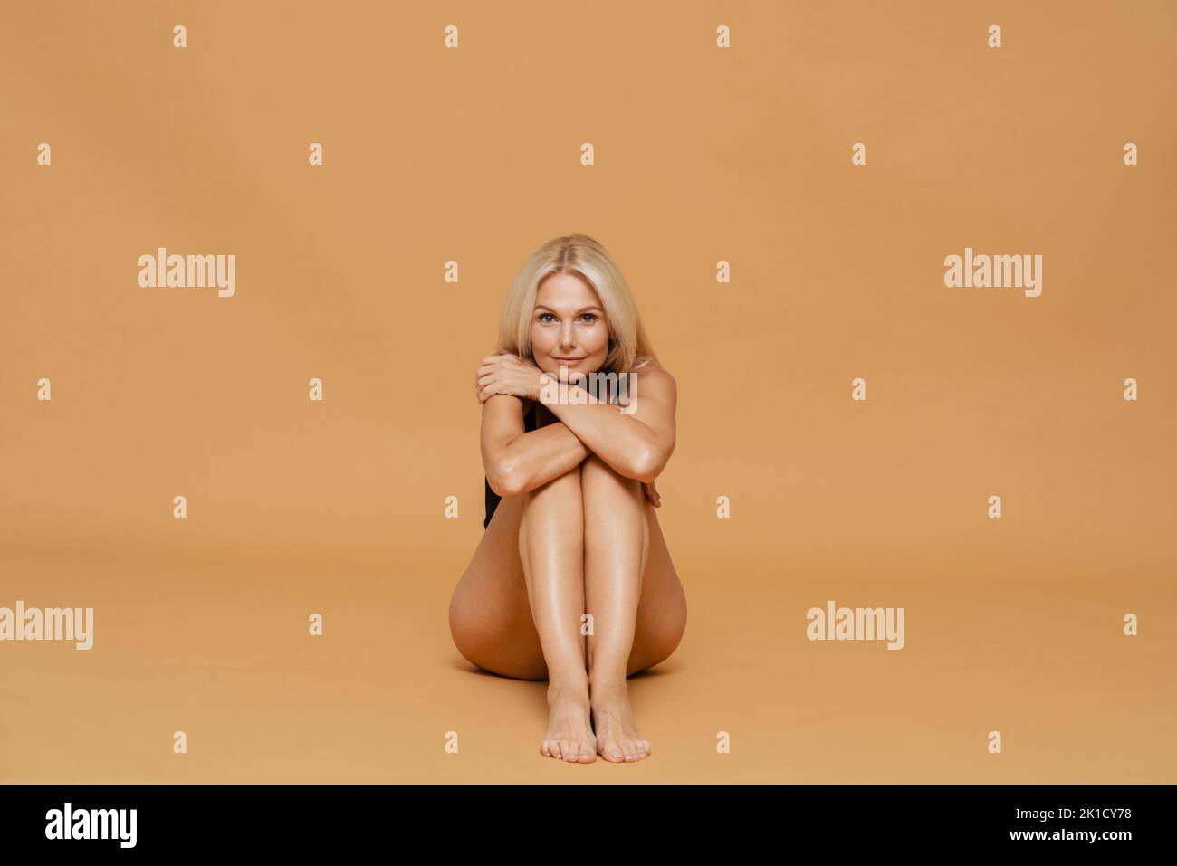 Mature blond beautiful woman wearing bodysuit smiling and posing at camera isolated over yellow background Stock Photo