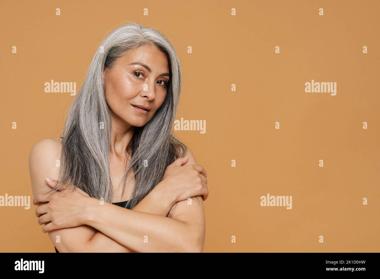 Mature asian beautiful woman wearing bodysuit smiling and posing at camera isolated over yellow background Stock Photo