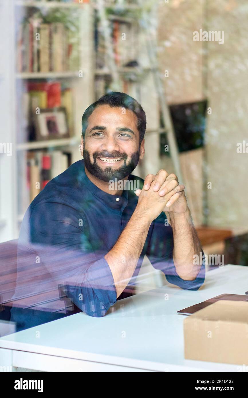 Successful happy indian business man looking away at work. View through glass Stock Photo