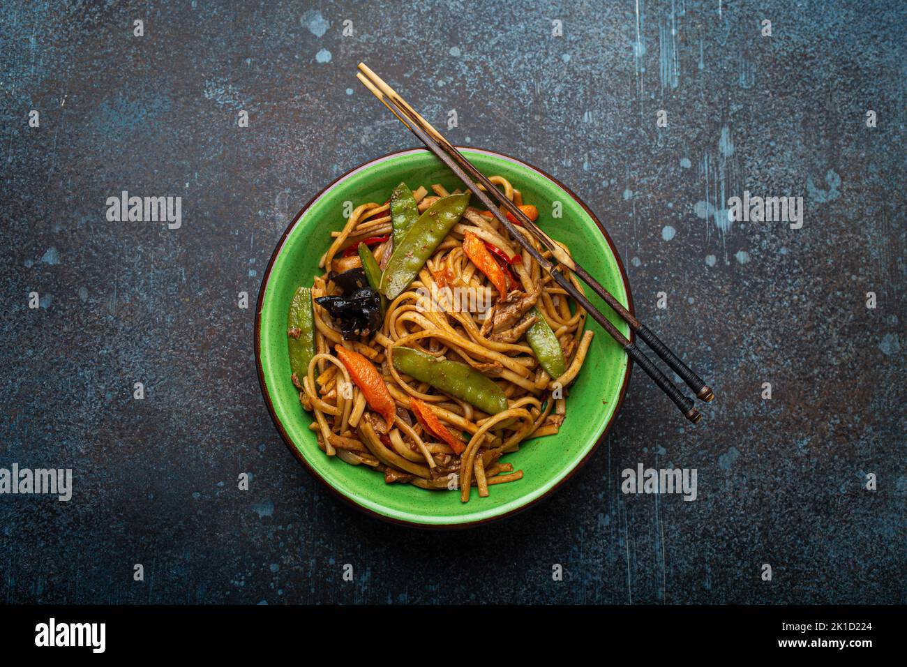 Asian stir fry noodles with chicken and veggies in green bowl top view Stock Photo