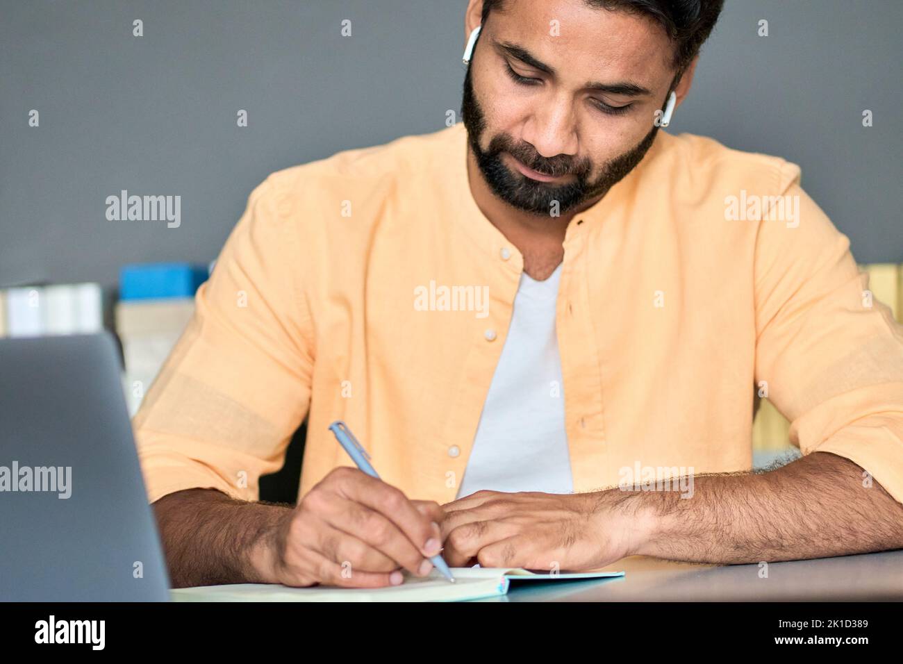 Indian man writing notes while learning online business education course. Stock Photo