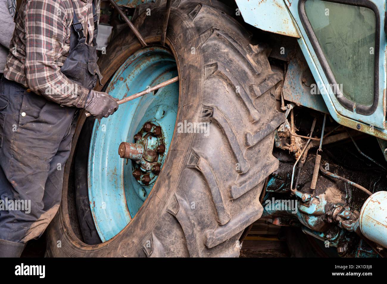 Change agricultural tractor broken tube tire at home. Man worker use crowbars to pry beneath the edge of the rim and break the bead. Stock Photo