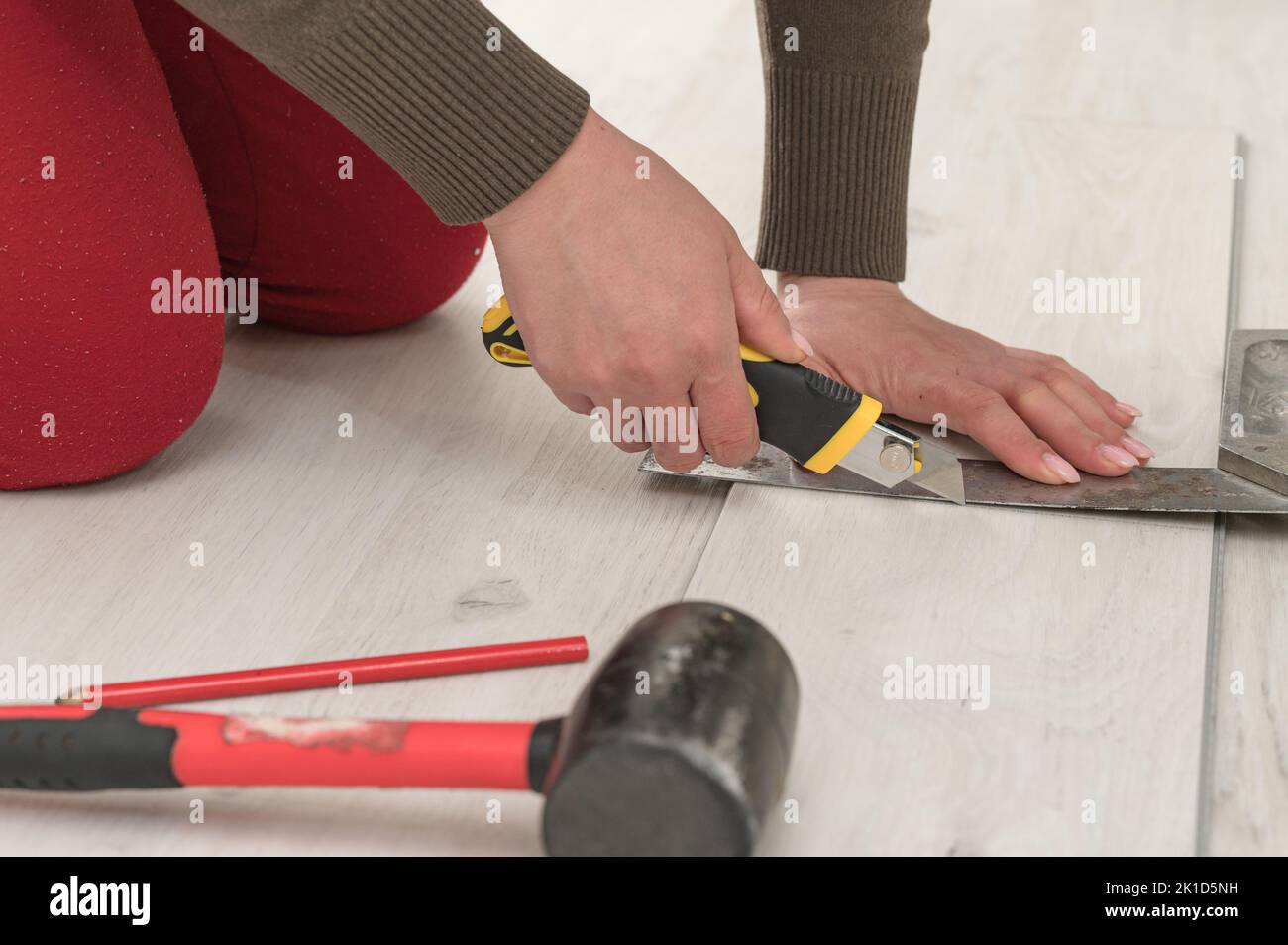 Female master cuts quartz vinyl floor with a stationery knife, floor installation, woman performs repair work. Stock Photo