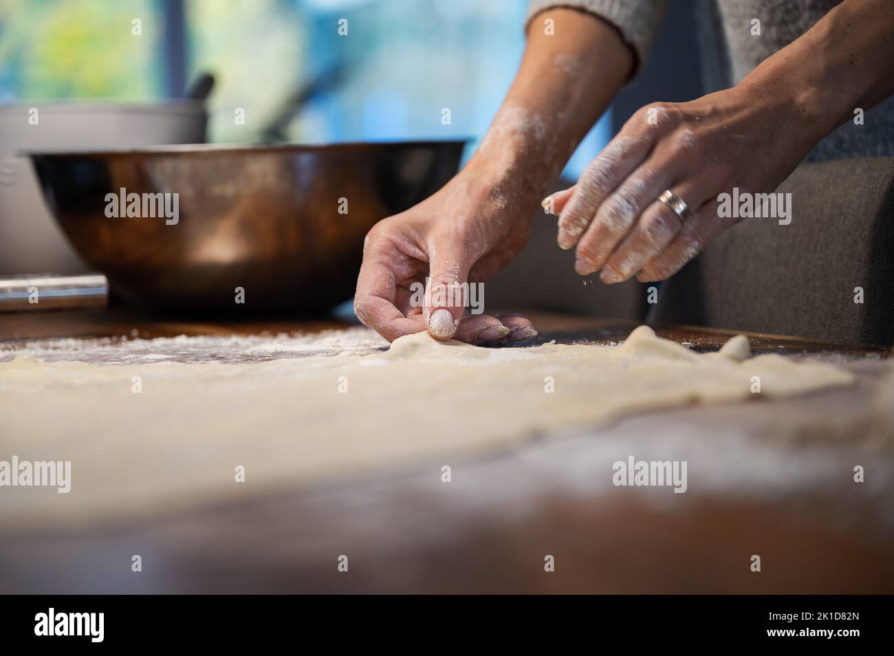 Low angle view of a woman preparing homemade pastry dough for a strudel or pie, stetching it on a flour dusted wooden table. Stock Photo