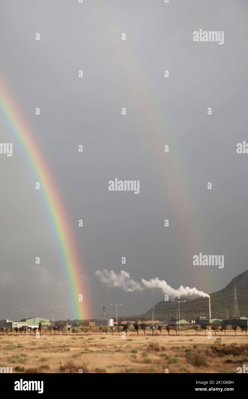 Double rainbow rising over an industrial area. Primary and secondary rainbows are visible Stock Photo