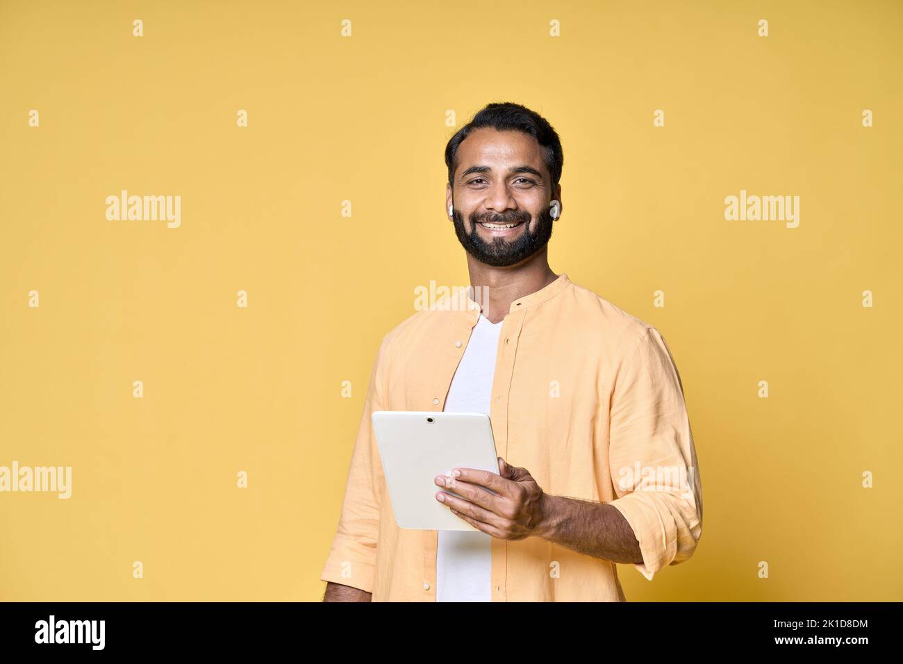Happy indian man using digital tablet isolated on yellow background. Stock Photo