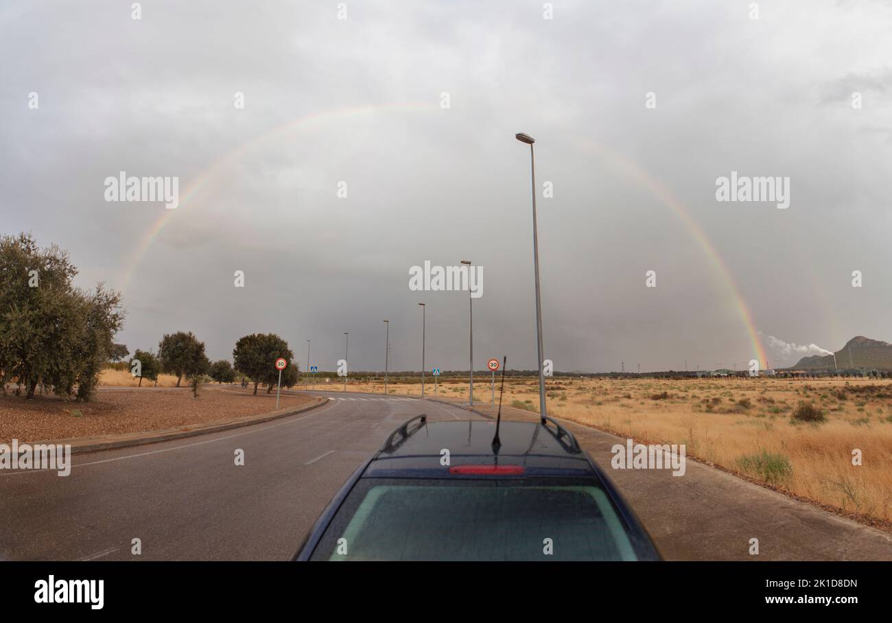Car at roundabout with rainbow rising over horizon. Industrial area Stock Photo