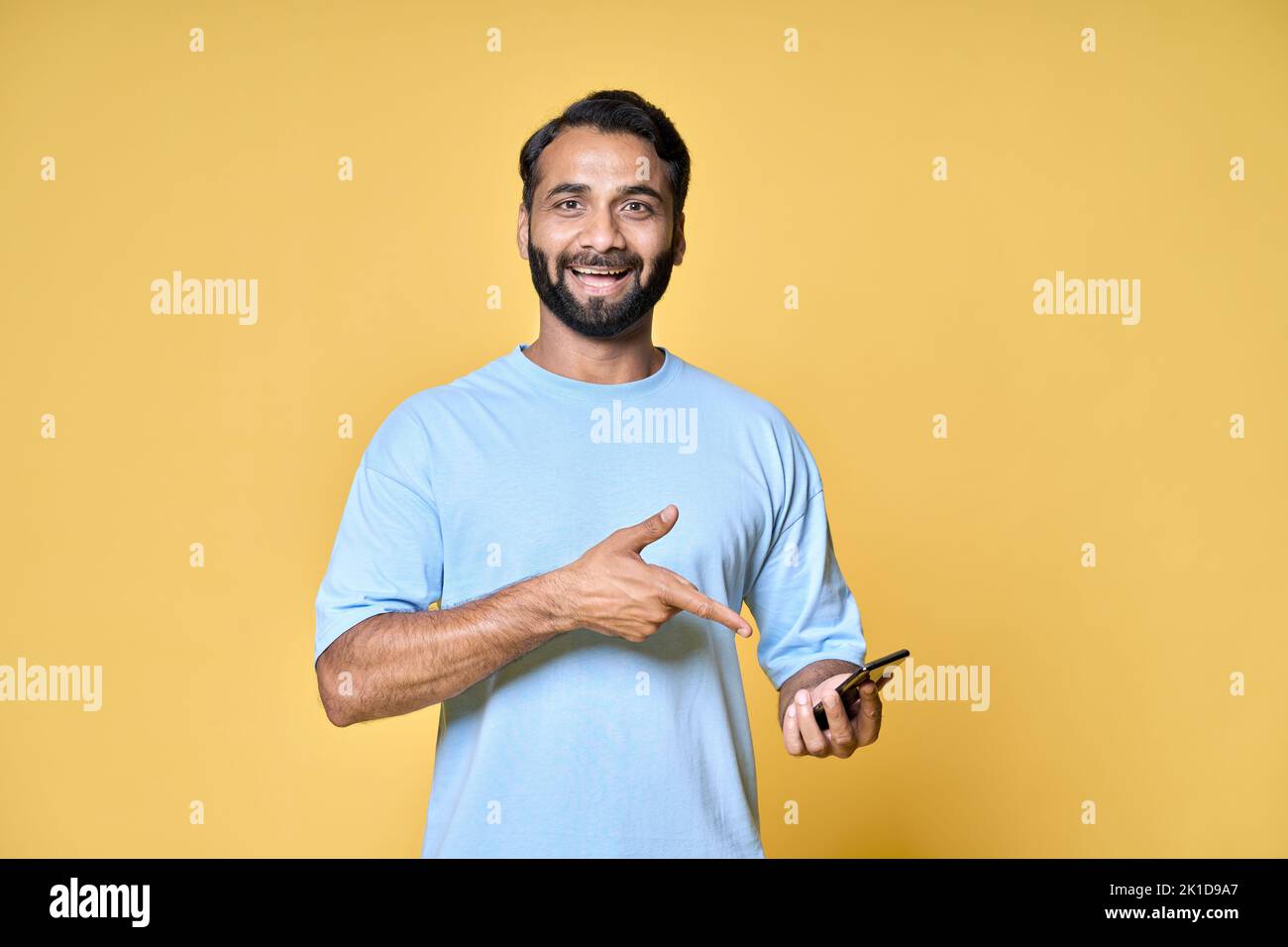 Happy indian man pointing at mobile phone isolated on yellow background. Stock Photo
