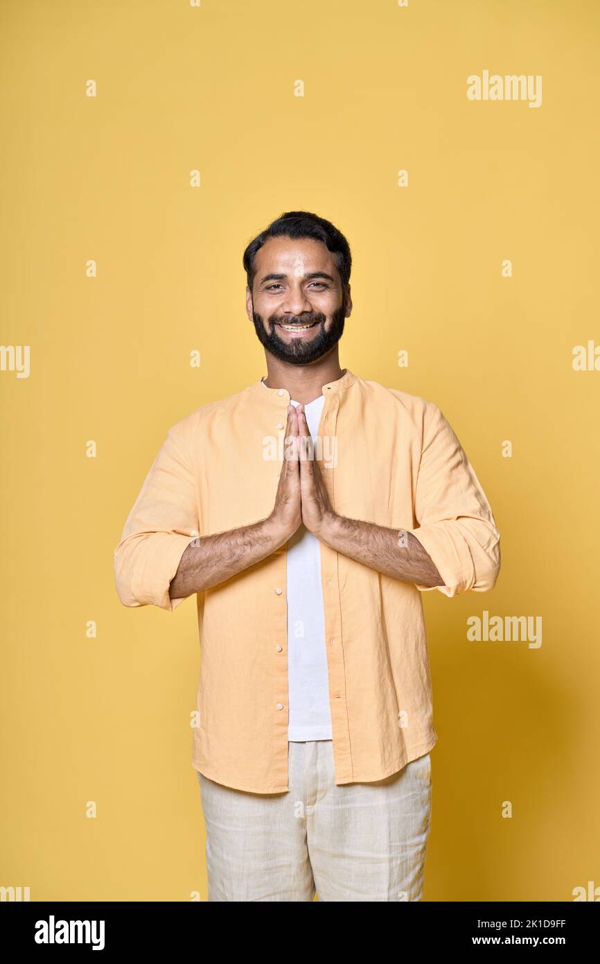 Happy indian man meditating holding hand in namaste isolated on yellow. Vertical Stock Photo