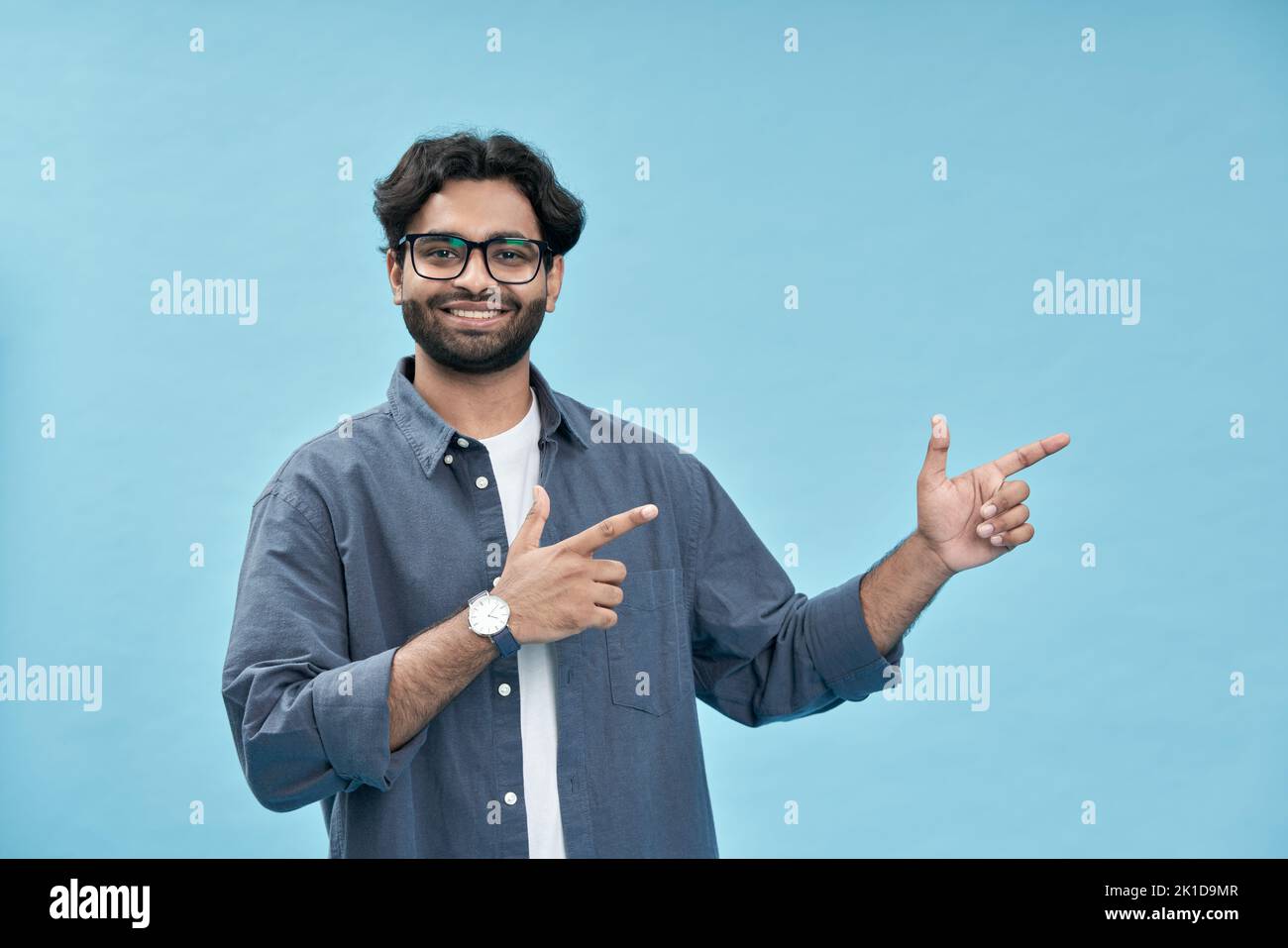 Happy young arab man pointing advertising commercial offer isolated on blue. Stock Photo