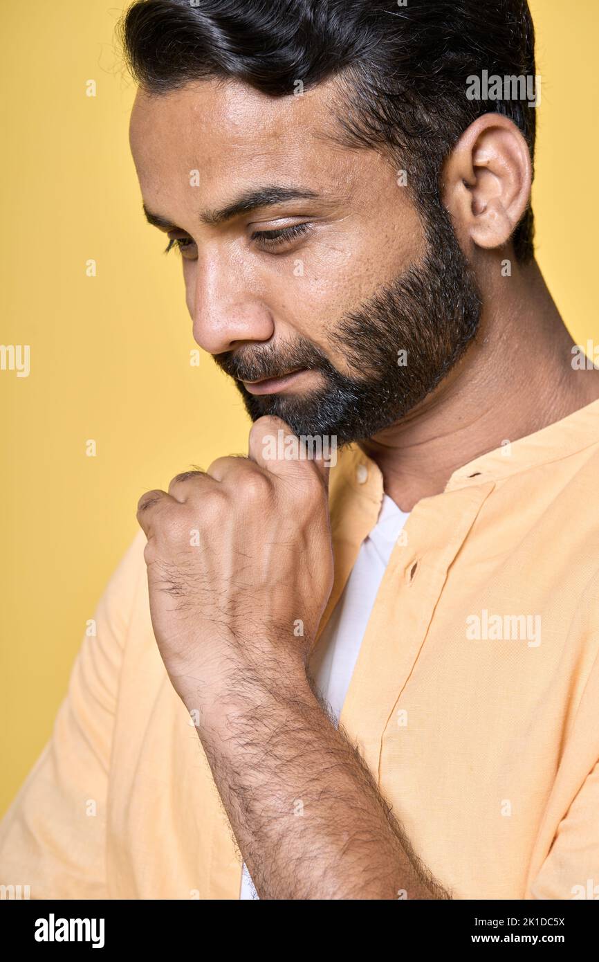 Smiling thoughtful indian man thinking isolated on yellow. Vertical portrait Stock Photo