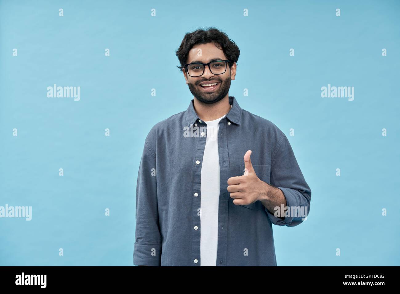 Smiling happy young arab man showing thumbs up isolated on blue background. Stock Photo