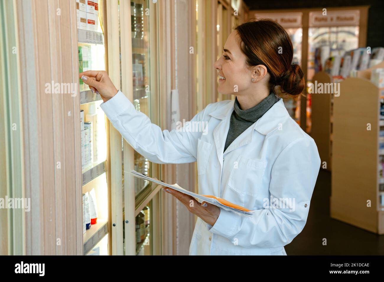 White pharmacist woman wearing medicine coat smiling while working in apothecary Stock Photo