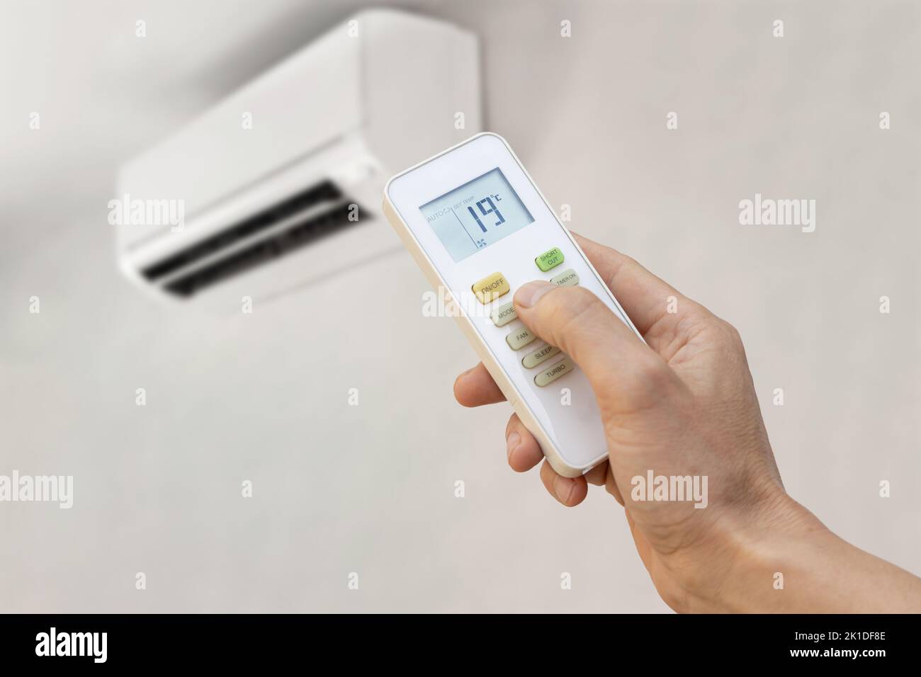 Hand with remote control of an air conditioner setting the temperature to 19 degrees. Energy saving concept. Stock Photo