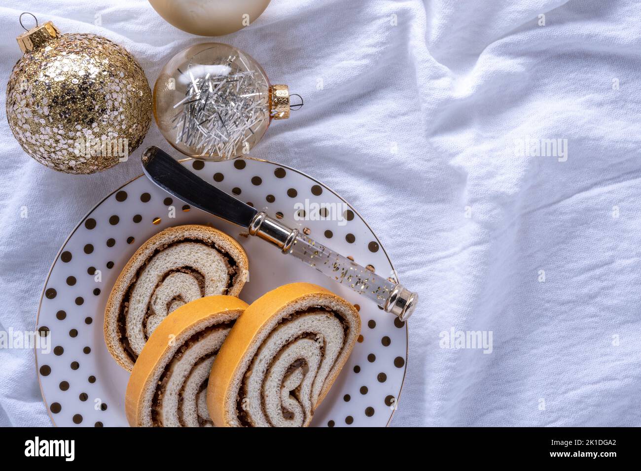 festive holiday dessert background with nut roll on a plate, spreader, and sparkly ball ornaments Stock Photo