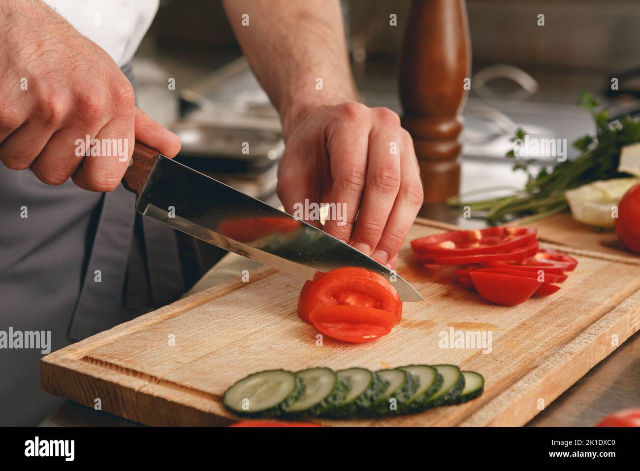 Busy chef cutting tomatoes and cucumbers on a board in modern restaurant kitchen Stock Photo