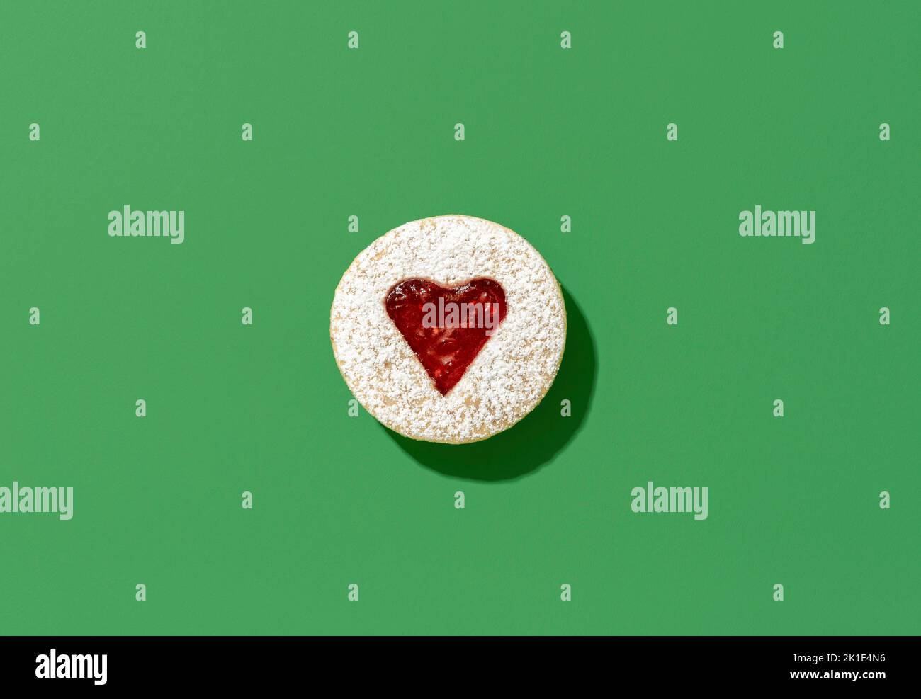 German traditional christmas sweets, linzer cookie, minimalist on a green table. Heart-shaped linzer cookie in bright light. Stock Photo
