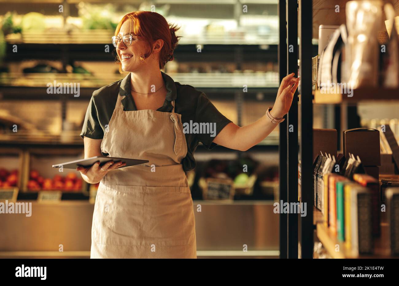 Successful shop owner smiling happily while holding a digital tablet in her grocery store. Cheerful female entrepreneur running a small business in th Stock Photo