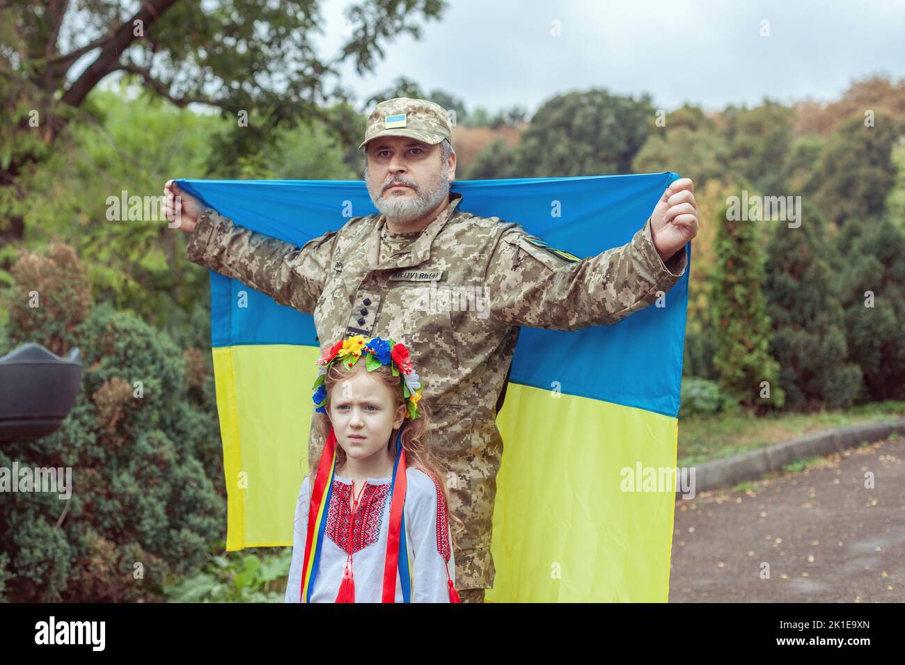 Portrait of a Ukrainian soldier with his little daughter. They stand with the flag of Ukraine. Stock Photo