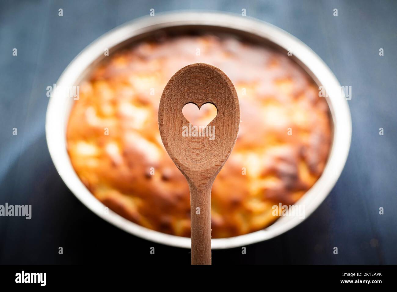 Wooden spoon with heart shaped hole, and pie in the background on blue table. Baked with love concept. Stock Photo
