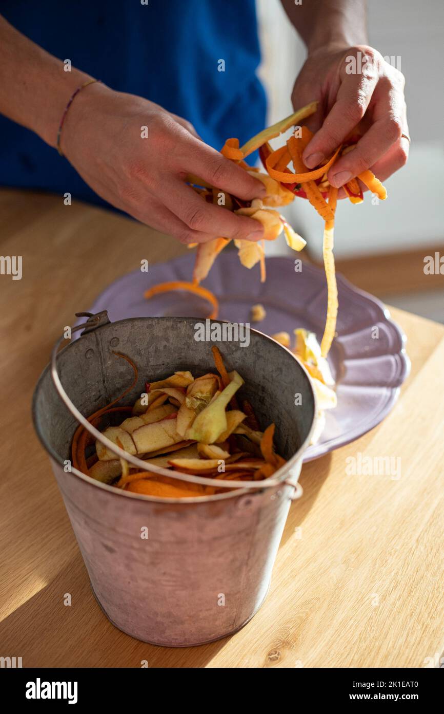 Male hands sorting vegetable peelings in tin bin. Use of food waste, composting, in order to enrich soil fertility. Garbage sorting at home. Vertical Stock Photo