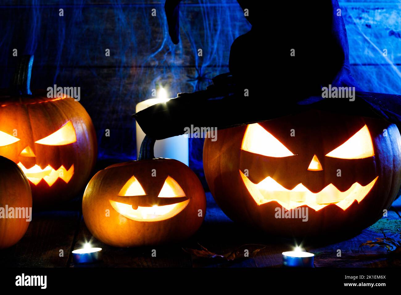Festive mystical halloween interior. Pumpkin, spider web, burning candles, spiders on dark wooden background Stock Photo