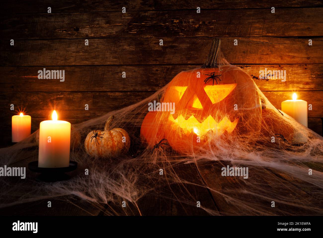 Festive mystical halloween interior. Pumpkin, spider web, burning candles, spiders on dark wooden background Stock Photo
