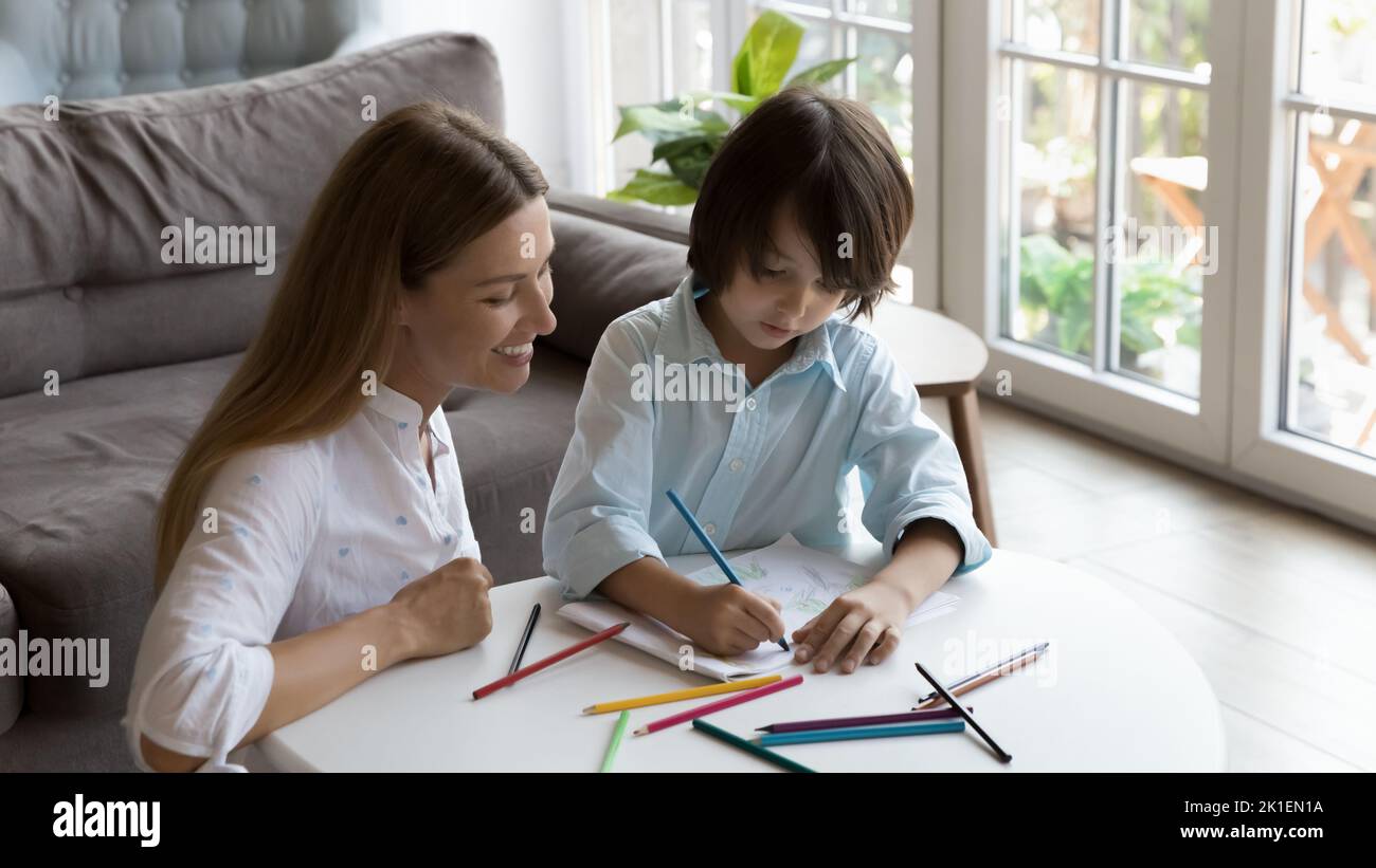 Happy loving mom watching kid drawing doodles in paper album Stock Photo