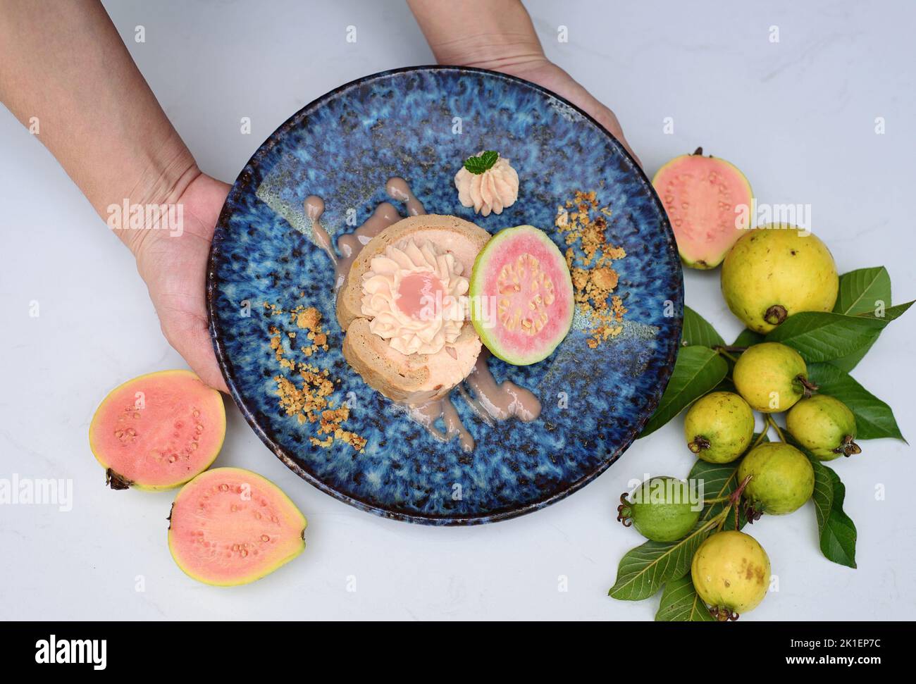 Hands holding plate with Guava Roll Cake on light background with ripe guava fruit Stock Photo