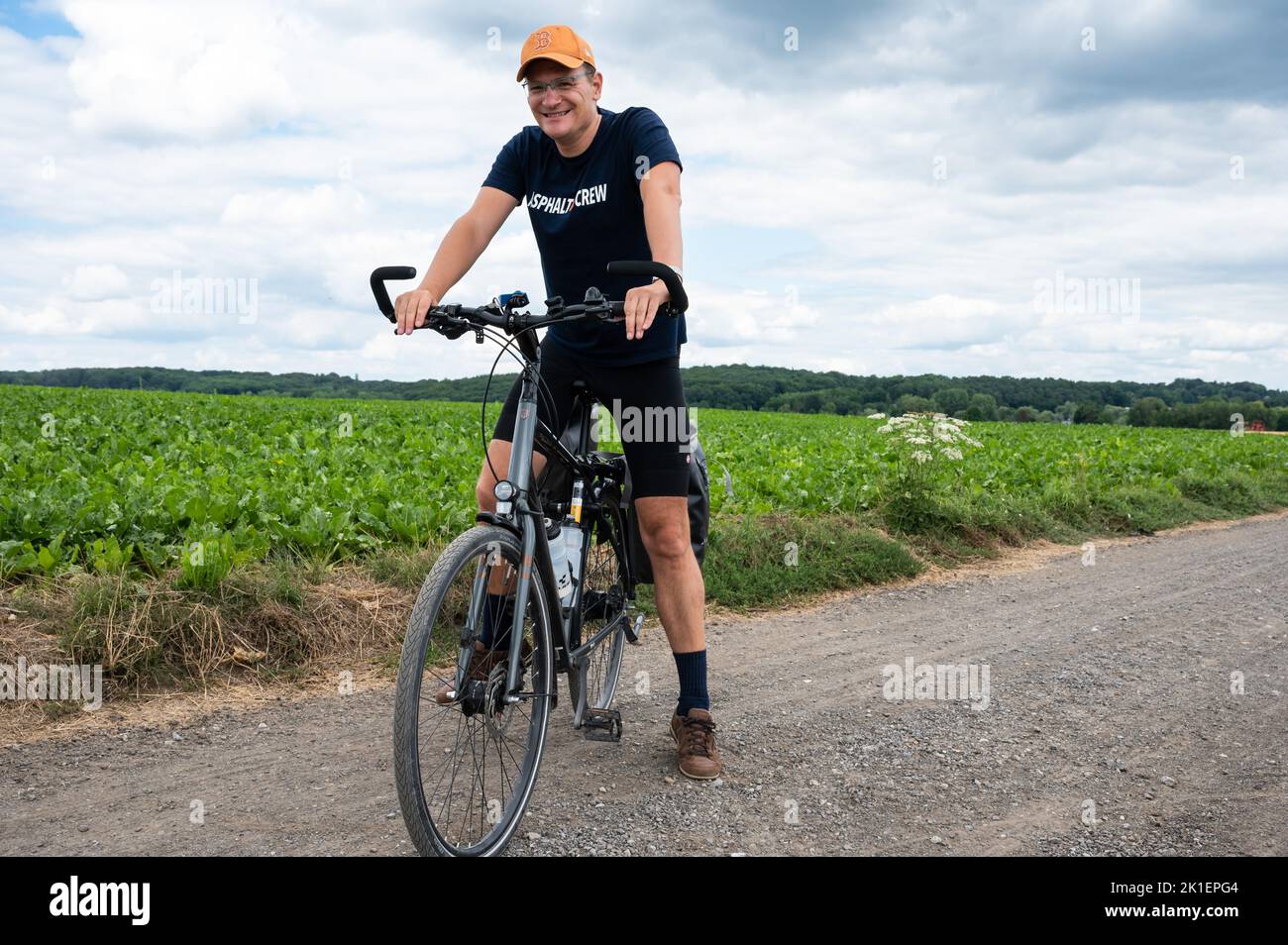 Bossut, Wallon Region, Belgium - 08 21 2022 - 40 yo man posing with his trekking bike in agricutlure fields Stock Photo